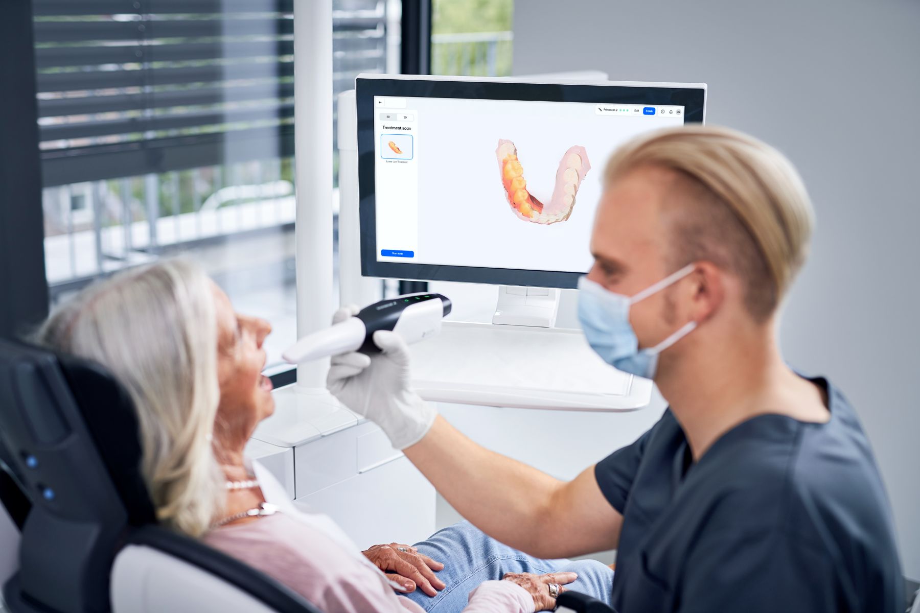 Zahnarzt erfasst den Kiefer einer Patientin mit einem Intraoralscanner, das Modell erscheint auf dem Bildschirm
